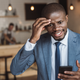 Angry African American businessman gesturing and using smartphone in cafe